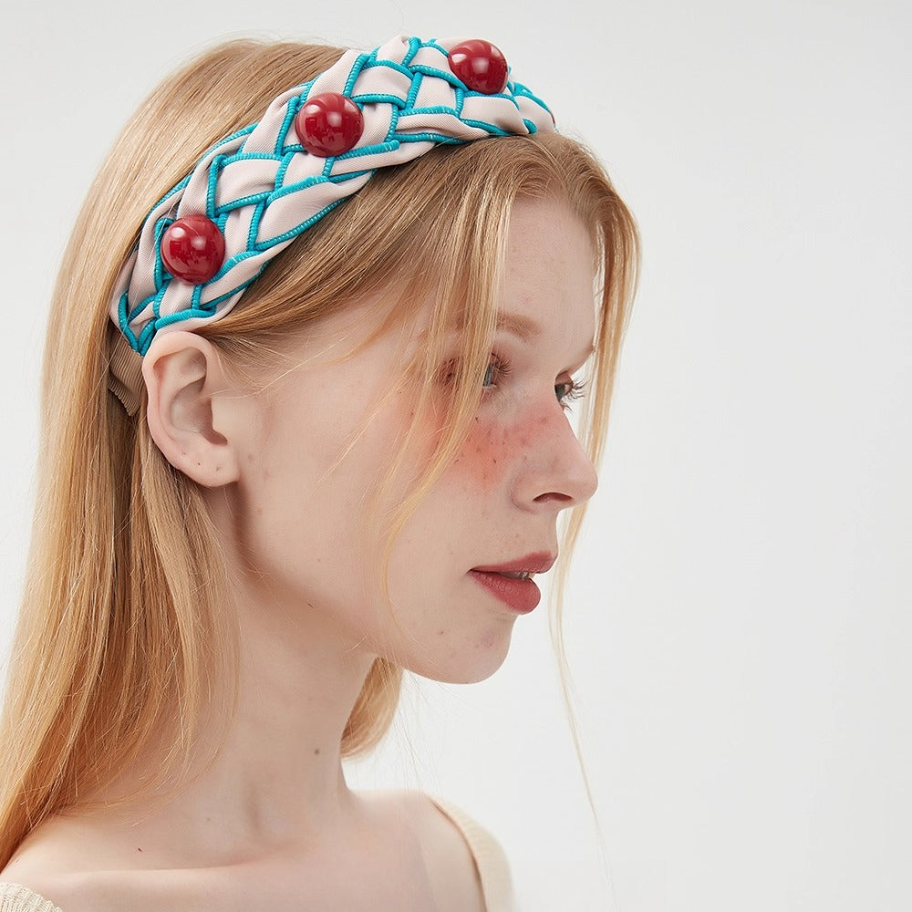 Women's embellished headband with beige and turquoise braided fabric and large red bead accents