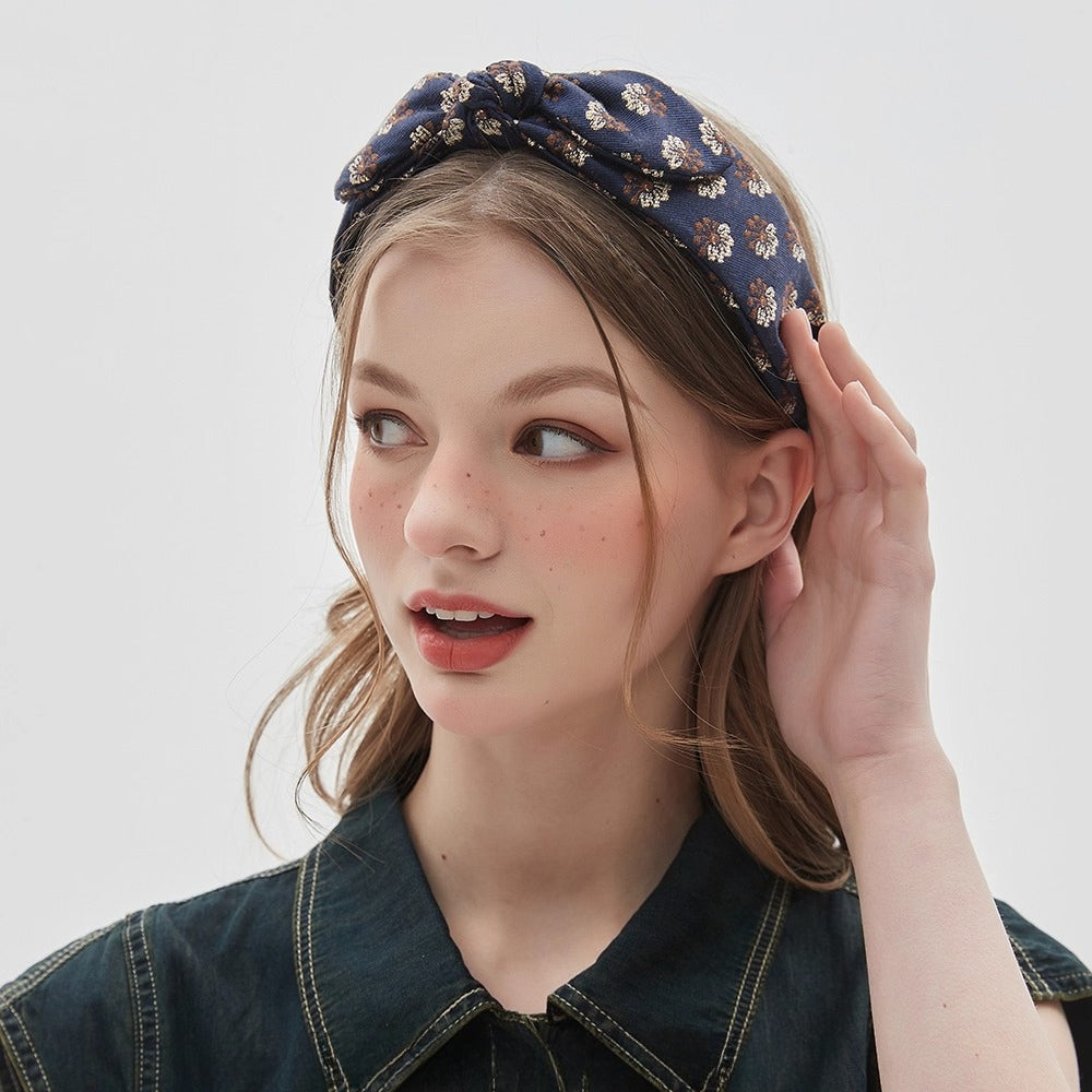 Navy blue printed bow headband with small floral pattern in beige and brown on woman