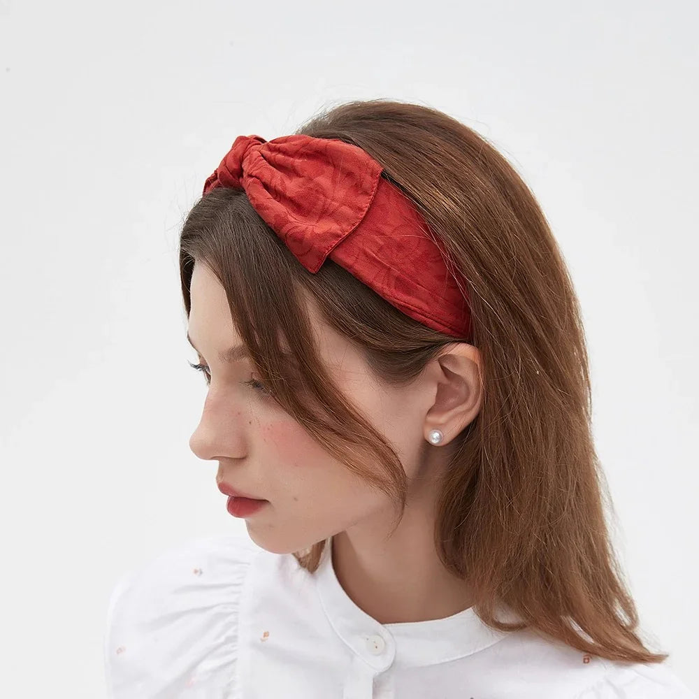 Women's red bow headband with subtle textured floral pattern, fabric material, embellished style